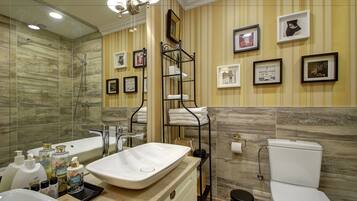 A modern bathroom with a bathtub, a sink, a toilet, and a shower. There are framed pictures on the wall and a shelf with towels.