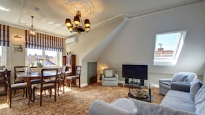 A living room with a dining area, a grey sofa, a TV, and a patterned carpet.