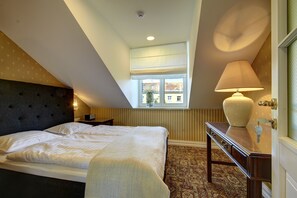 Une chambre à coucher comprenant un lit, une table de chevet, une lampe, une commode et une fenêtre donnant sur des immeubles.