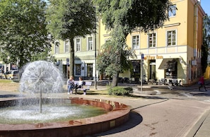 A public square with a fountain, benches, and a building with a sign for a coffee shop.