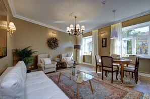 A living room with a sofa, chairs, a glass coffee table, a chandelier, and a view of the outdoors through a window. - German 18 - Luxury Vilnius Apartment (Vilnius)