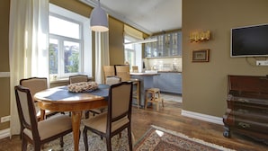A dining area with a round table, chairs, and a rug. There is a kitchen in the background with cabinets and a television.
