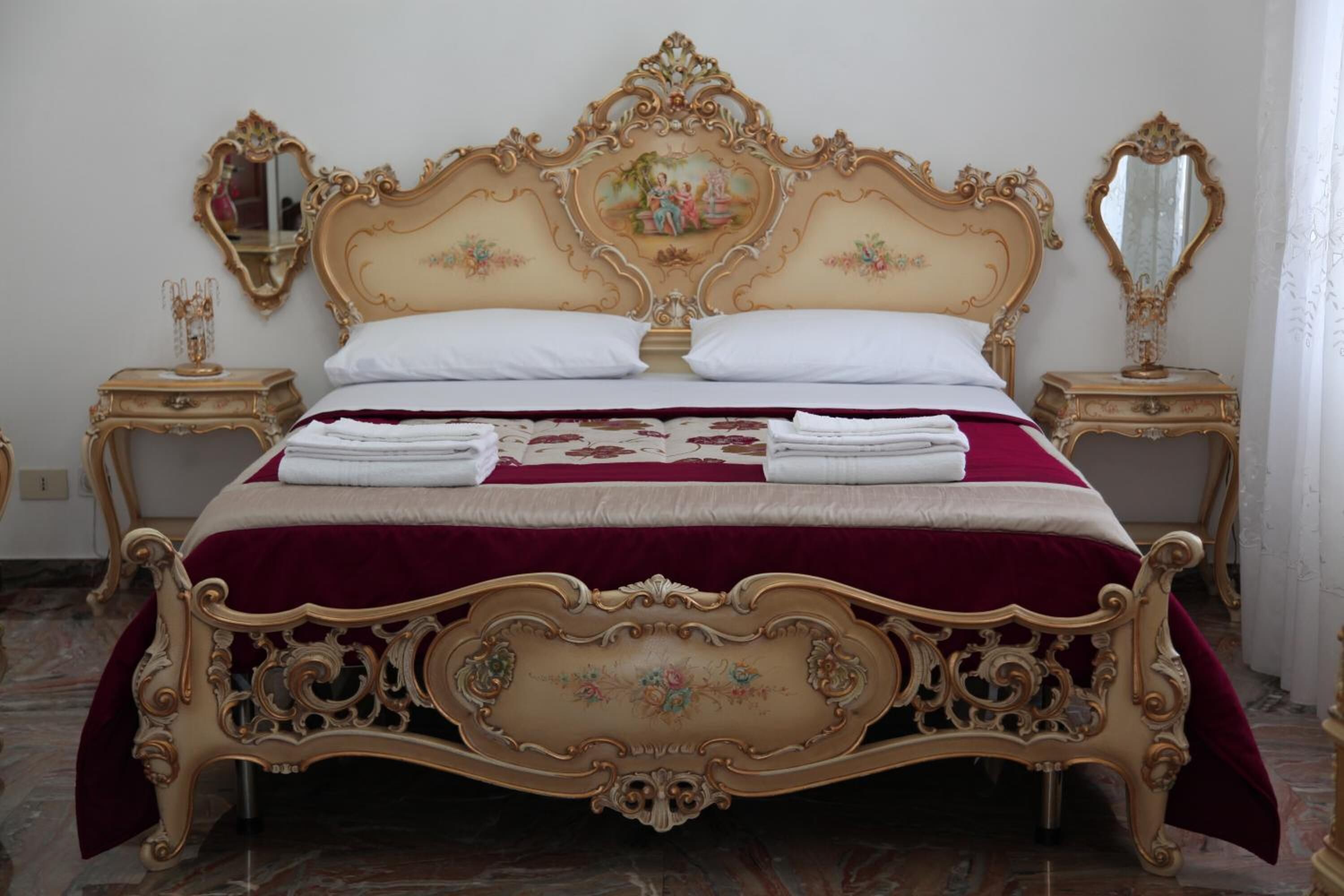 Un lit à baldaquin classique, agrémenté de motifs dorés raffinés, de draps blancs et d’une couvre-lit rouge.