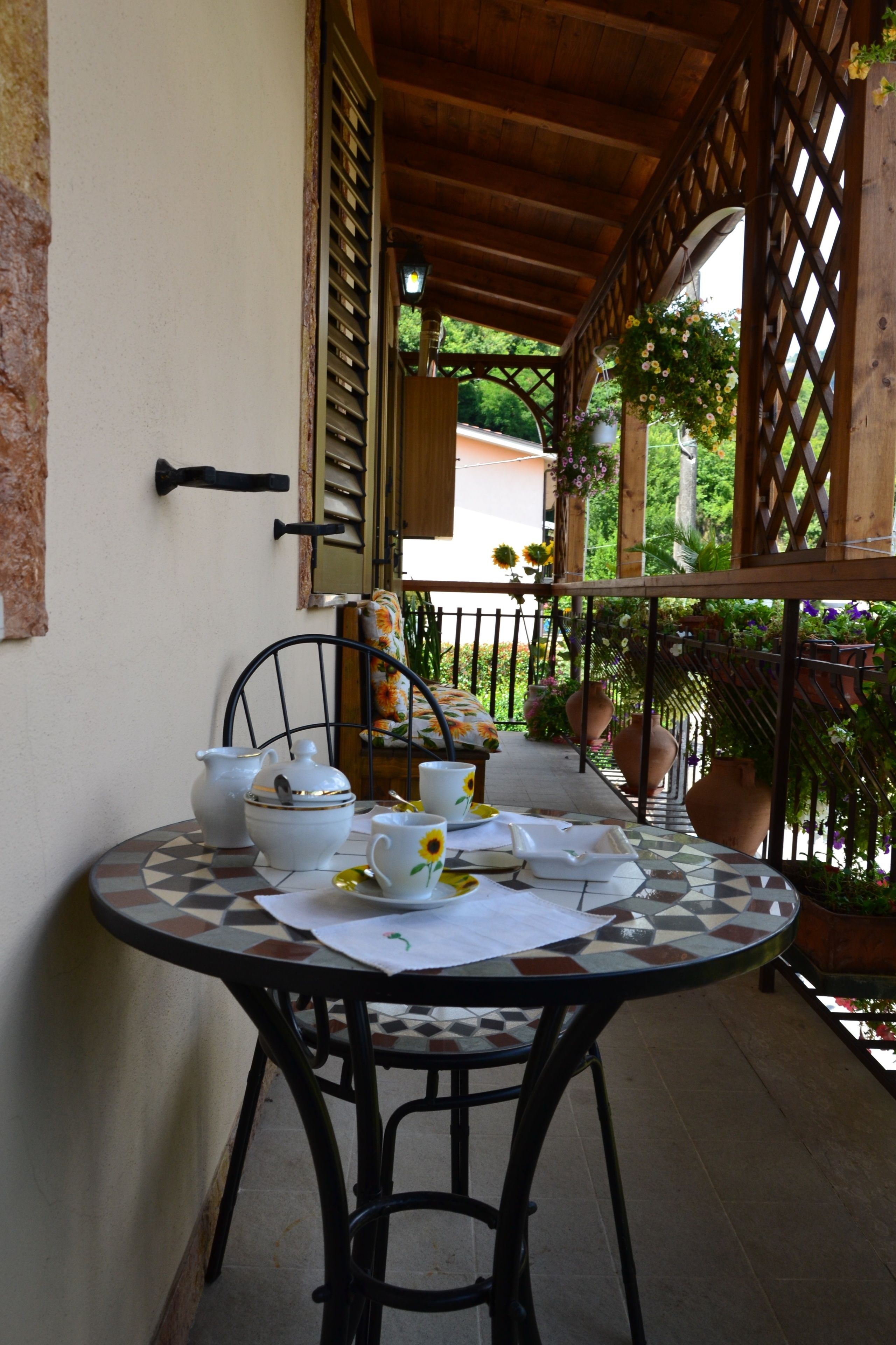 A round table with a checkered tablecloth, a metal chair, and a set of white ceramic tea set.