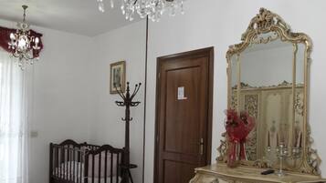 Una camera d'albergo con una culla, un comò con uno specchio, un lampadario e un letto con copripiumino floreale.