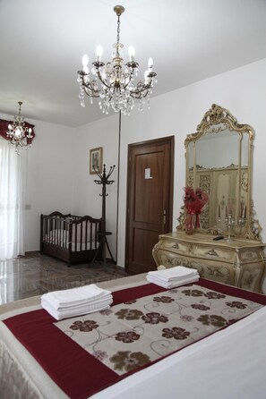 A hotel room with a crib, a dresser with a mirror, a chandelier, and a bed with a floral bedspread.