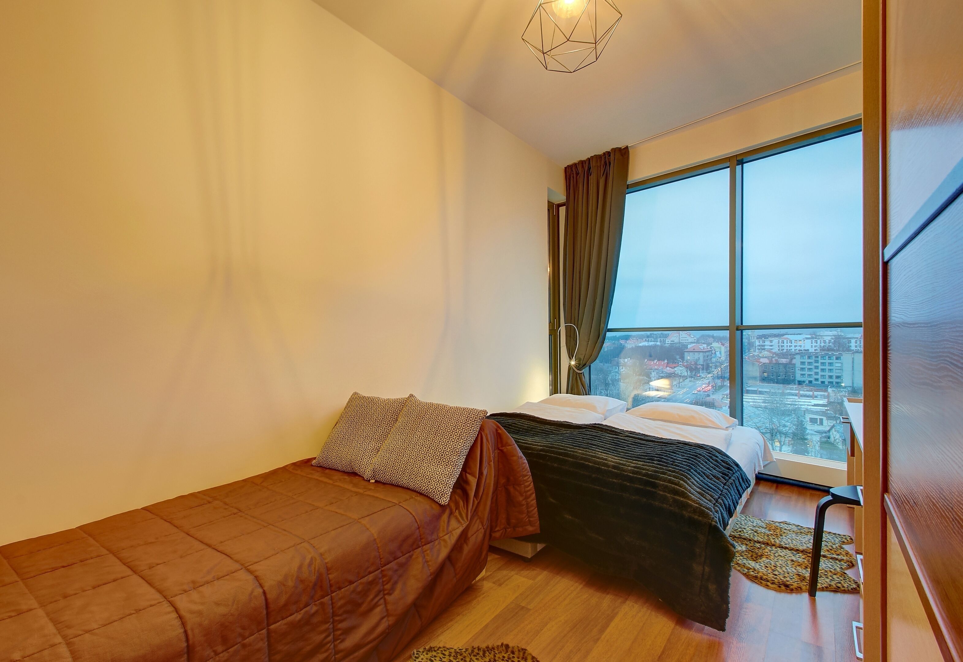 Un dormitorio con dos camas, un ventanal con cortinas y vistas a la ciudad.