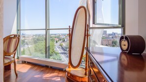A room with a large window, a wooden chair, a dresser, and a mirror. - Helios City Vilnius Apartments (Vilnius)