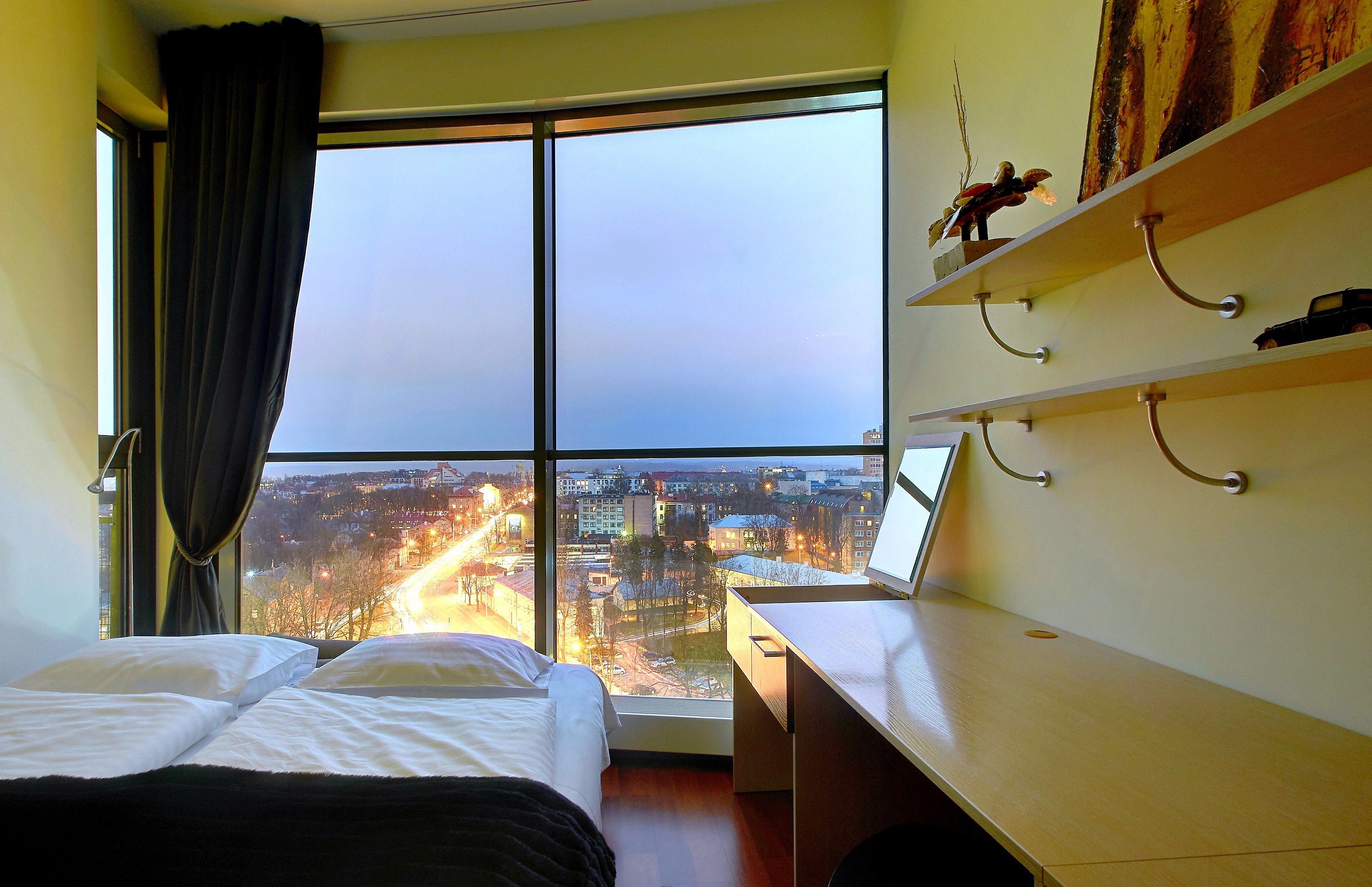 Hotellihuone, jossa on suuri ikkuna, sänky, työpöytä ja näkymä kaupunkimaisemaan.