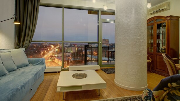 A modern living room with a large window, a sofa, a coffee table, and a cabinet. - Helios City Vilnius Apartments (Vilnius)
