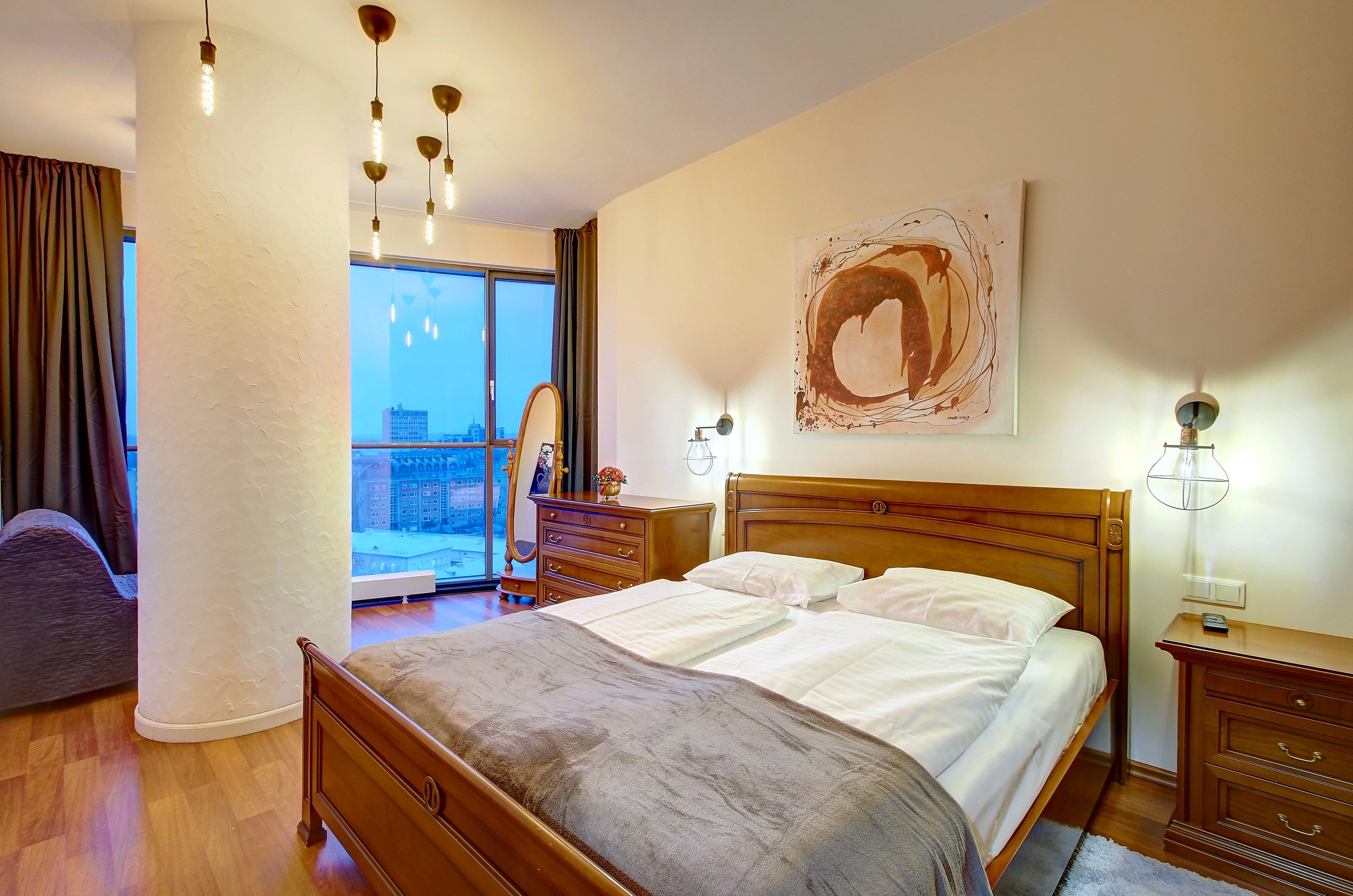Une chambre d’hôtel avec un grand lit, une commode, une table de chevet, un miroir et une vue sur la ville par une grande fenêtre.