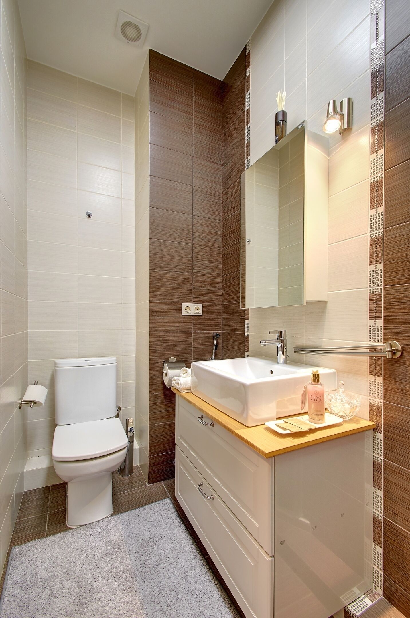 Een moderne badkamer met een wit toilet, een wastafel met spiegel en een houten opbergmeubel.
