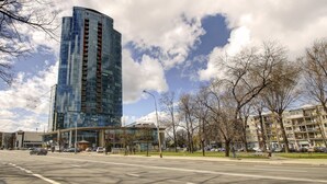 A modern high-rise building with a glass facade, located at a city intersection with a clear sky and some clouds. - Helios City Vilnius Apartments (Vilnius)