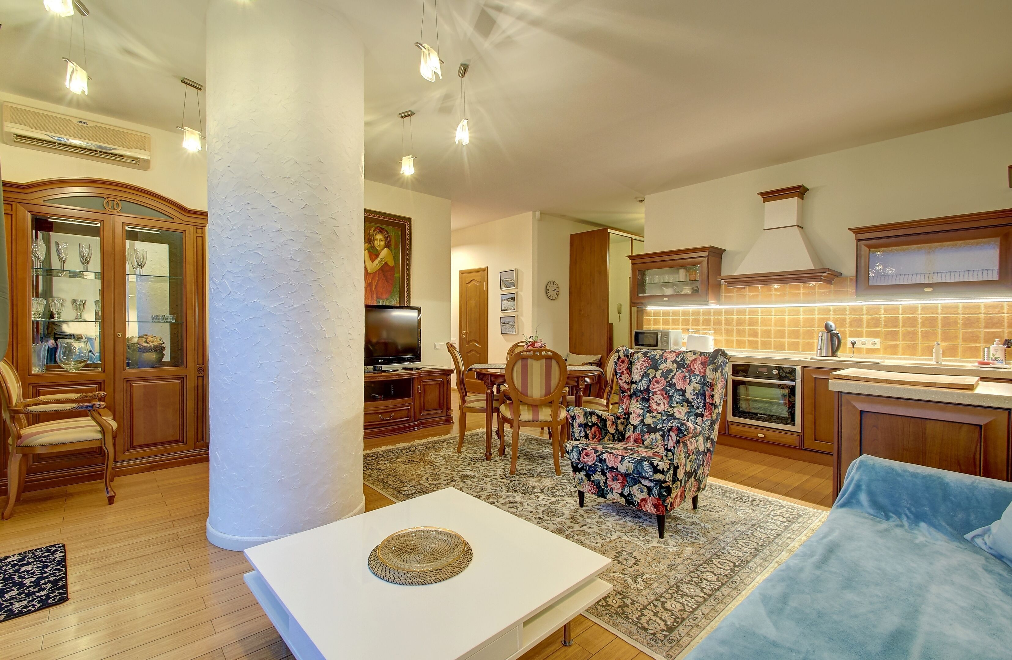 A spacious living area with a dining set, a television, and a kitchen area with a tiled backsplash.