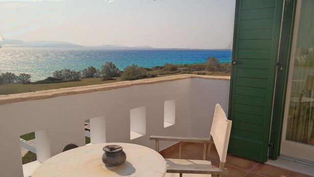 Ein Balkon mit rundem Tisch und Stuhl, der Blick auf die Küste mit Meer und entfernten Bergen freigibt.