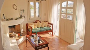 Ein gemütliches Wohnzimmer mit Kamin, einem Holzsofa, einem Couchtisch und Blick ins Freie durch ein großes Fenster.