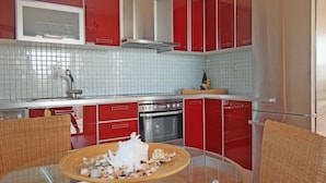 Eine moderne Küche mit roten Schränken, einem Edelstahlbackofen und einem Glastisch mit Dekoration.