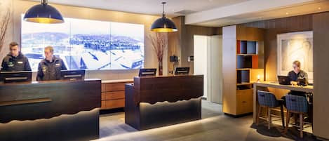 A modern reception area with a large desk, two receptionists, a computer, and a view of a snowy landscape.