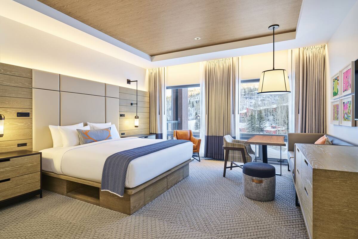 Une chambre d’hôtel moderne, dotée d’un grand lit, d’un bureau et offrant une vue sur un paysage enneigé.