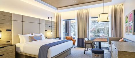 A modern hotel room with a large bed, a desk, and a view of a snowy landscape.