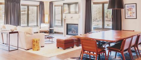 A spacious living room with a fireplace, a dining area with a large wooden table and chairs, and a cozy seating area with a sofa and ottomans.