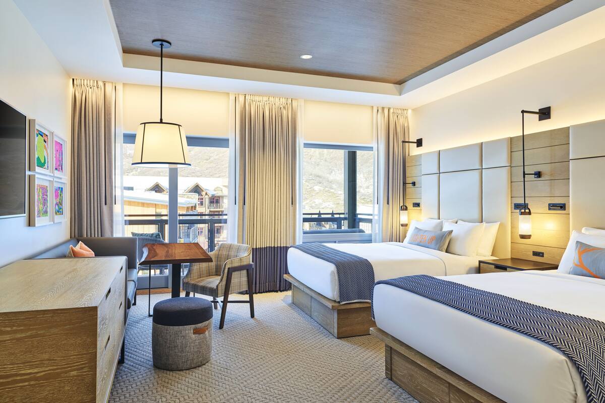 Une chambre d’hôtel comprenant un lit, des tables de chevet, un bureau, une chaise, une lampe et une vue sur l’extérieur.