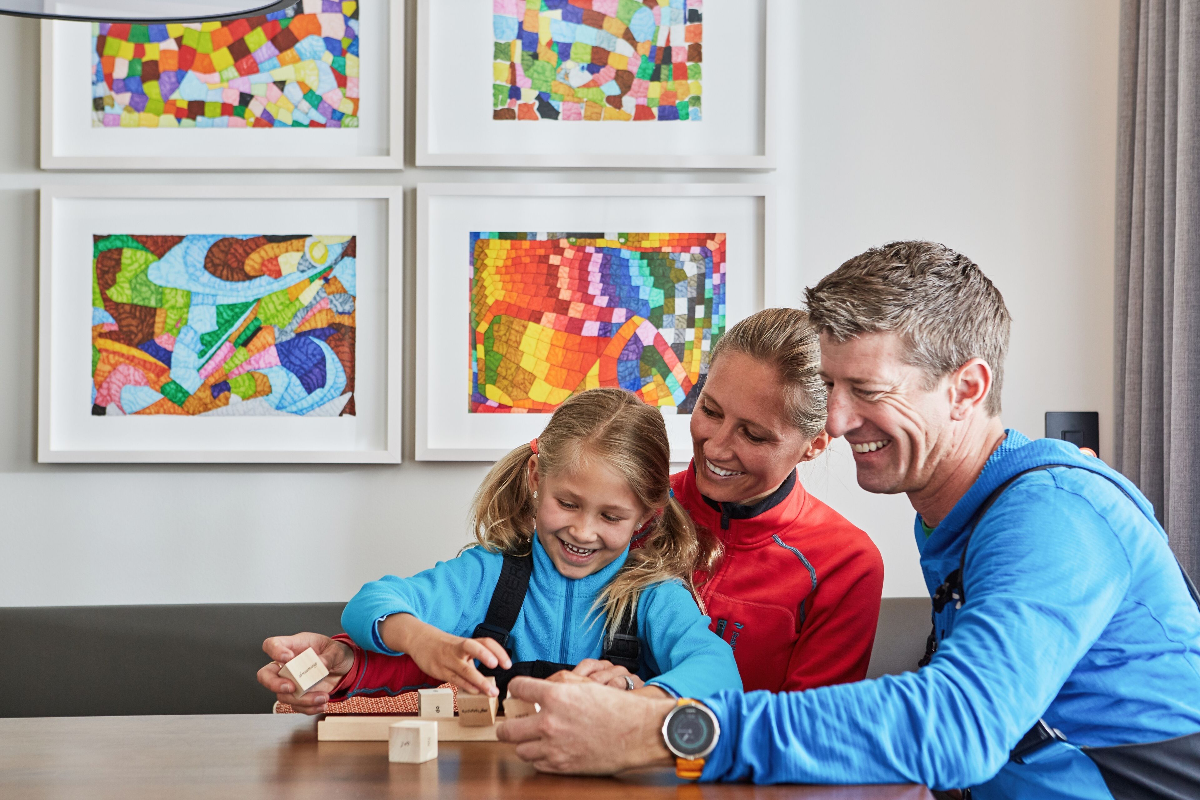 A family at a table with a puzzle, in a room with colorful abstract art on the wall.
