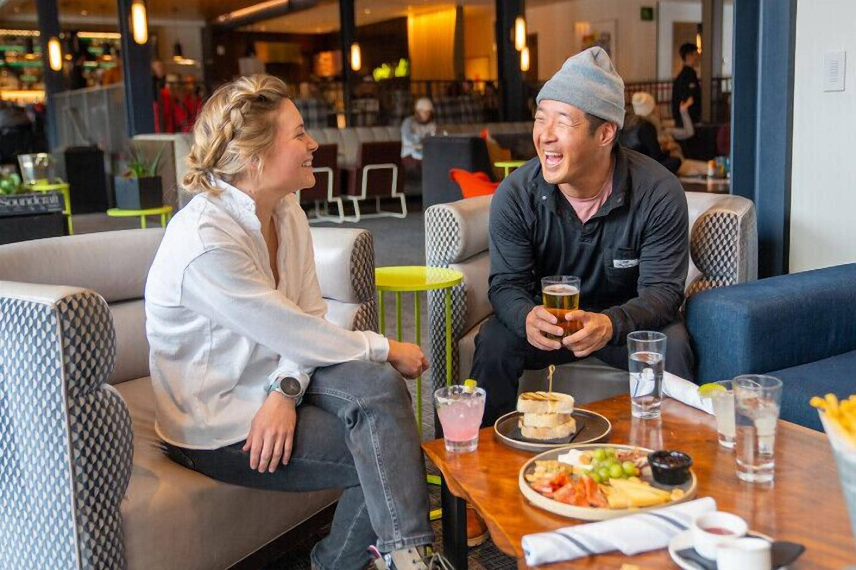 A couple sitting at a table in a modern cafe with a variety of food and drinks.