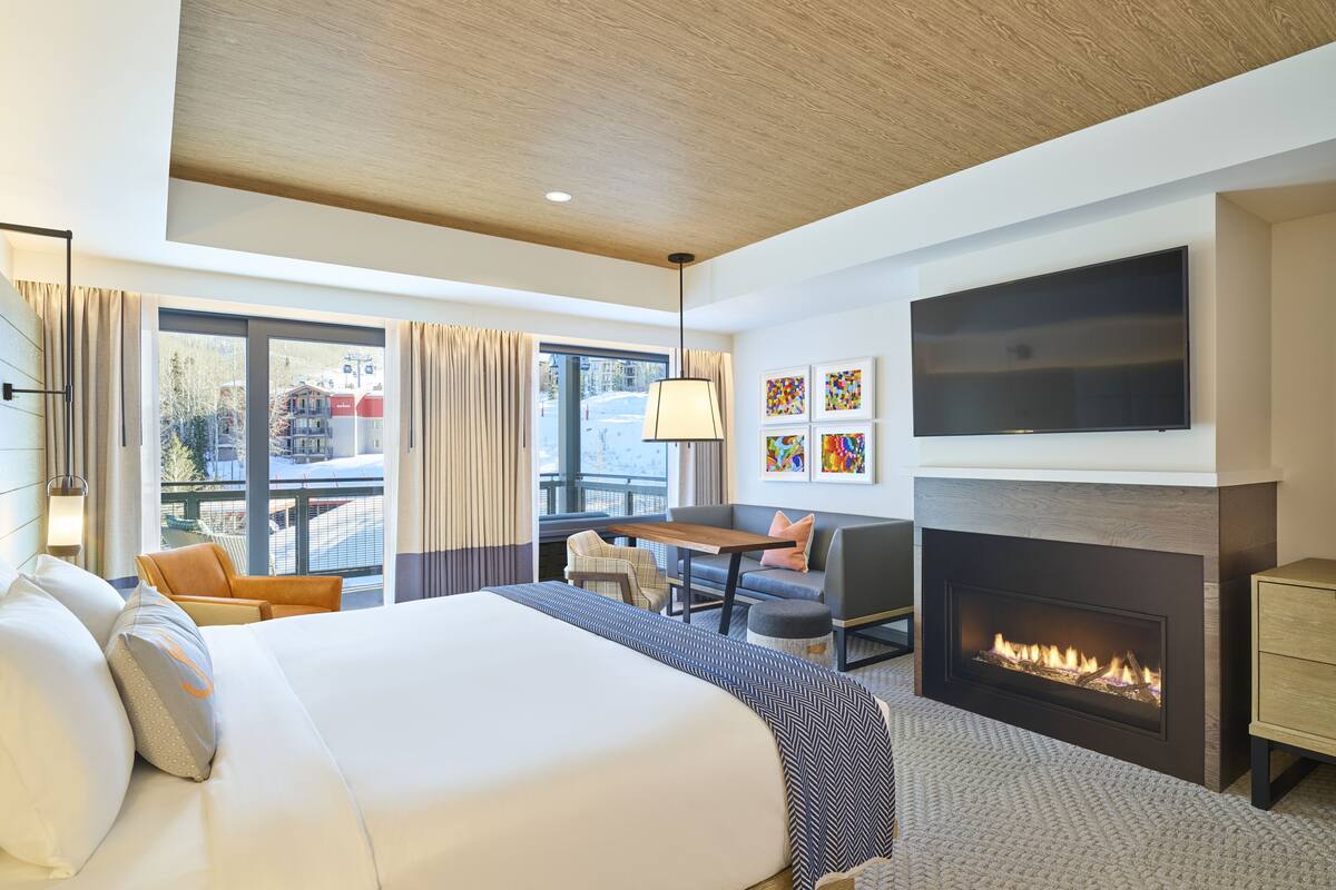 Une chambre d’hôtel moderne dotée d’un grand lit, d’une cheminée, d’une télévision à écran plat et d’un balcon offrant une vue sur l’extérieur.