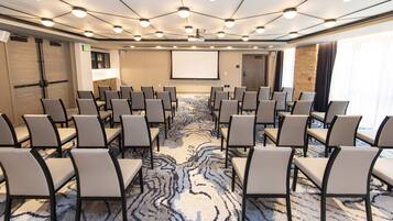 A conference room with rows of chairs, a projector screen, and a carpeted floor.
