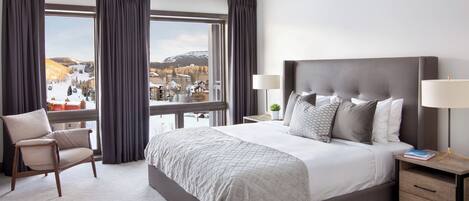 Une chambre d’hôtel avec un grand lit, une chaise, une table de chevet avec une lampe et une vue sur un paysage enneigé.