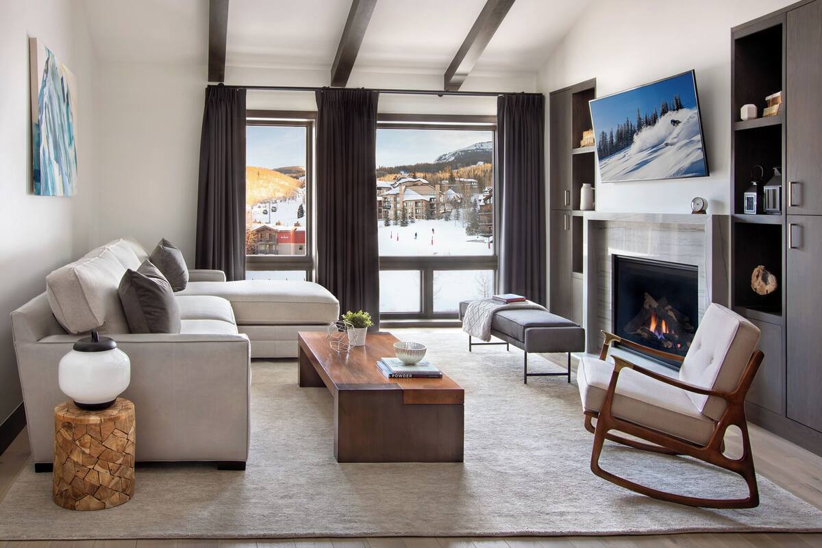 Un salon moderne avec un canapé, une table basse, une cheminée et une vue sur un paysage enneigé.
