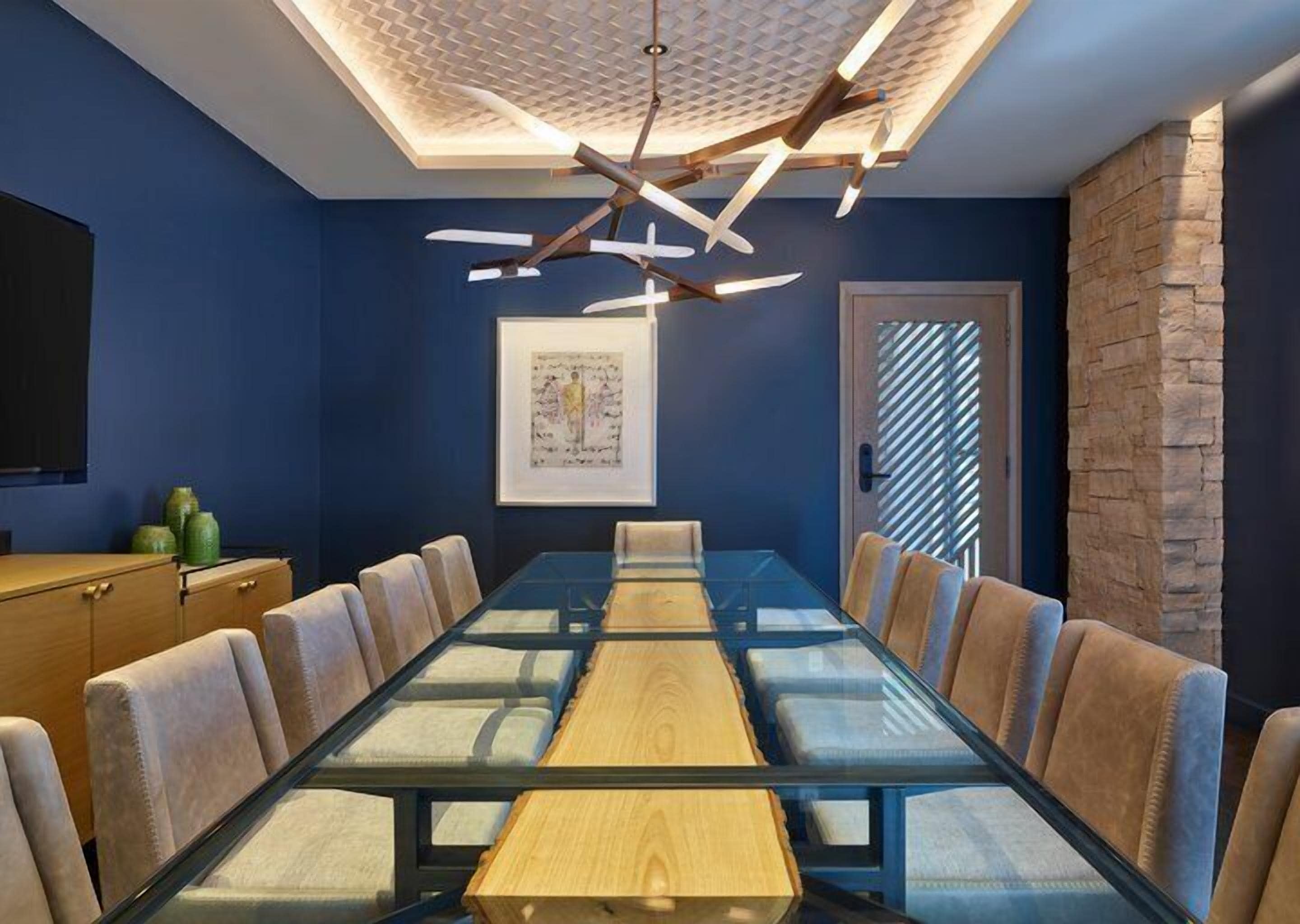 A conference room with a glass table, beige chairs, a wooden cabinet, and a framed artwork on the wall.