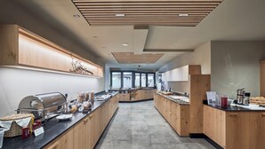 A spacious kitchen with wooden cabinets, a built-in grill, and a long counter with various food items. - Vinumhotel Feldthurnerhof (Velturno)