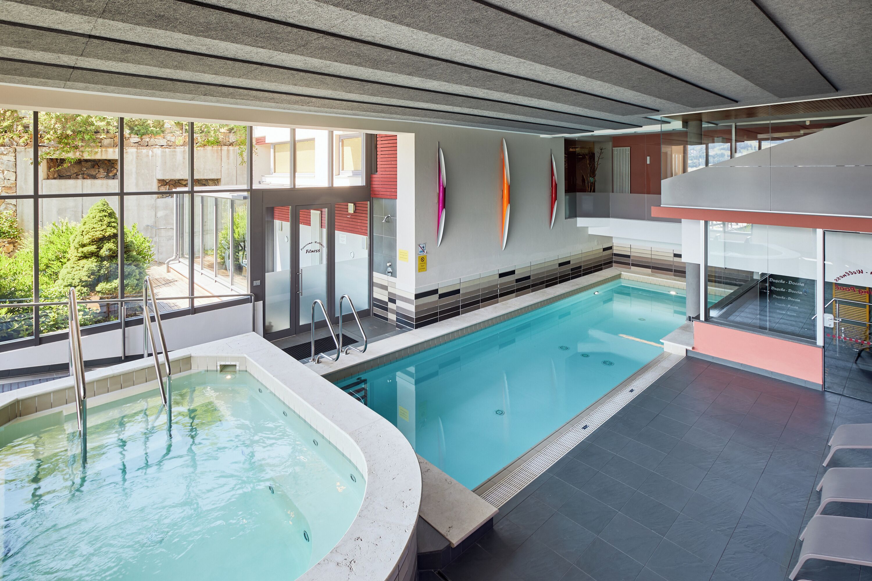 Une piscine intérieure avec des parois en verre transparent, un espace séparé avec un jacuzzi, et une vue sur l’extérieur.