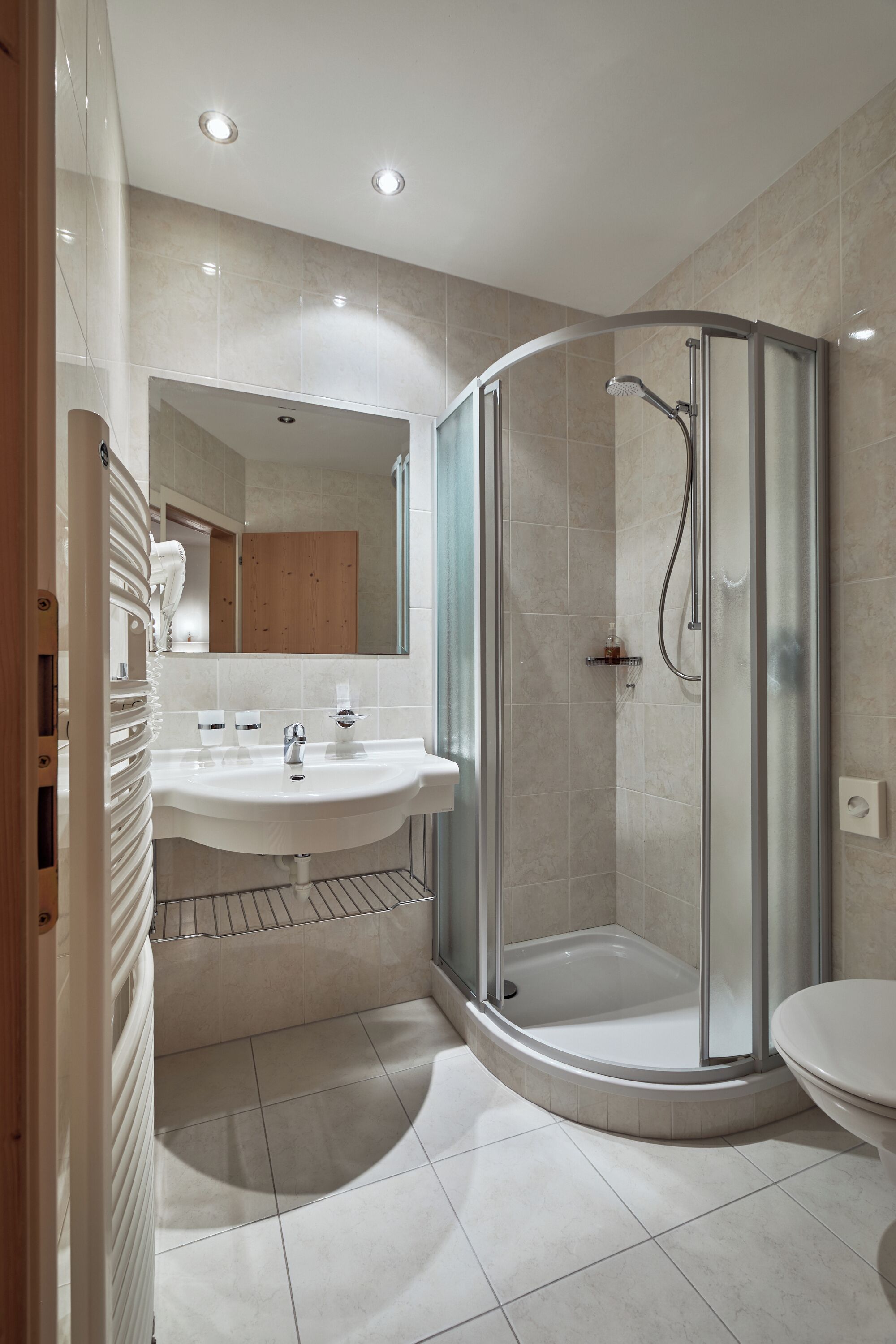 Een moderne badkamer met een glazen douchecabine, een witte wastafel en een toilet.