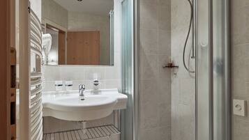 Een moderne badkamer met een glazen douchecabine, een witte wastafel en een toilet.