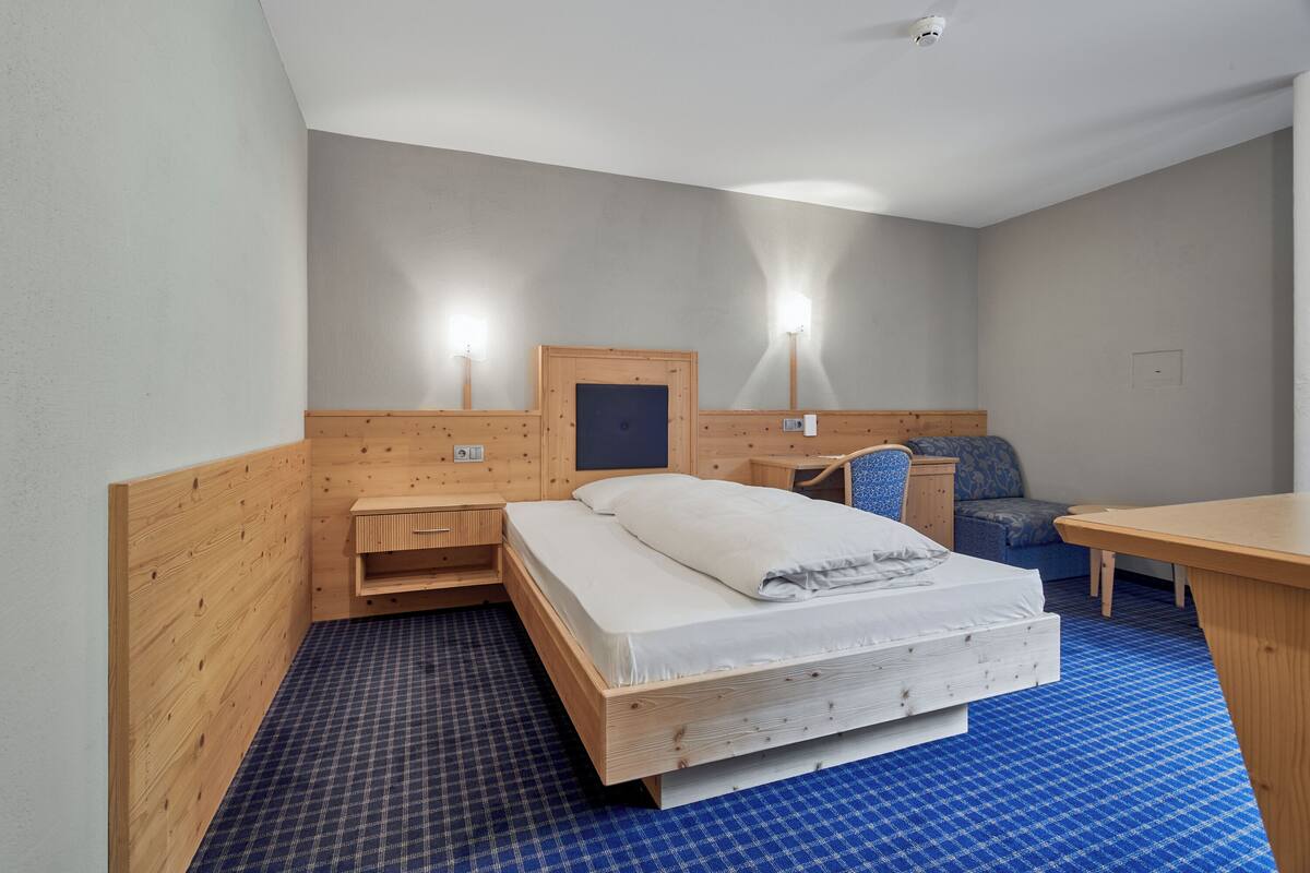 A hotel room with a wooden bed, a desk, and two wall-mounted lamps.