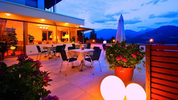 An outdoor dining area with a table and chairs, potted plants, and a view of mountains in the background. - Vinumhotel Feldthurnerhof (Velturno)