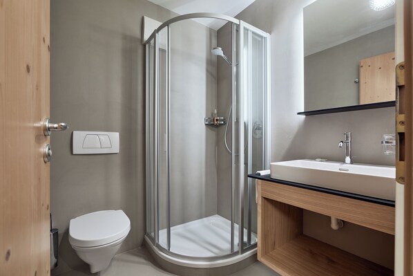 A modern bathroom with a glass-enclosed shower, a white toilet, and a wooden vanity with a sink.