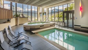A modern indoor pool area with a hot tub, seating, and large windows offering mountain views. - Vinumhotel Feldthurnerhof (Velturno)