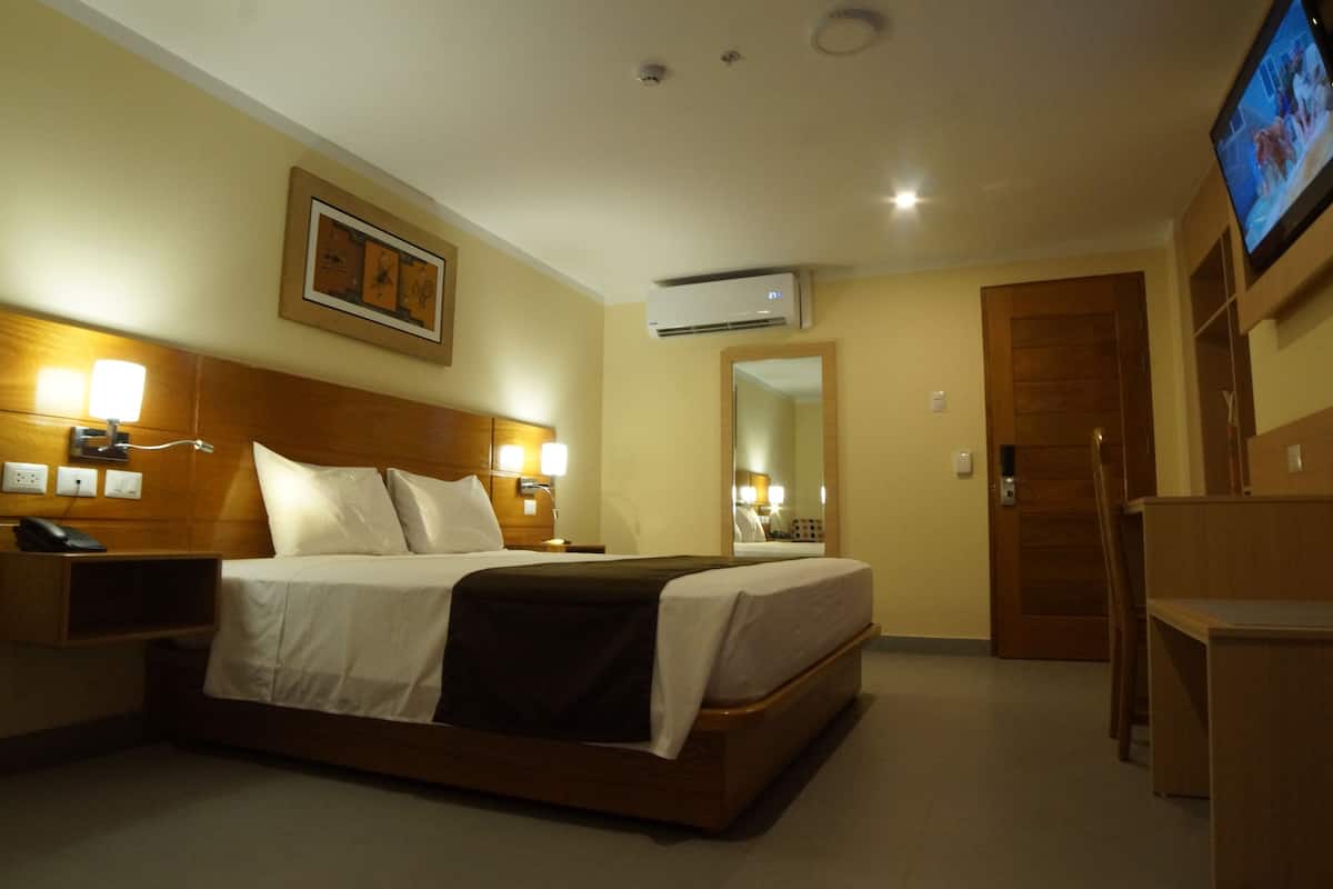 Une chambre d’hôtel équipée d’un lit, de lampes de chevet, d’un climatiseur, d’une télévision et d’une armoire en bois.
