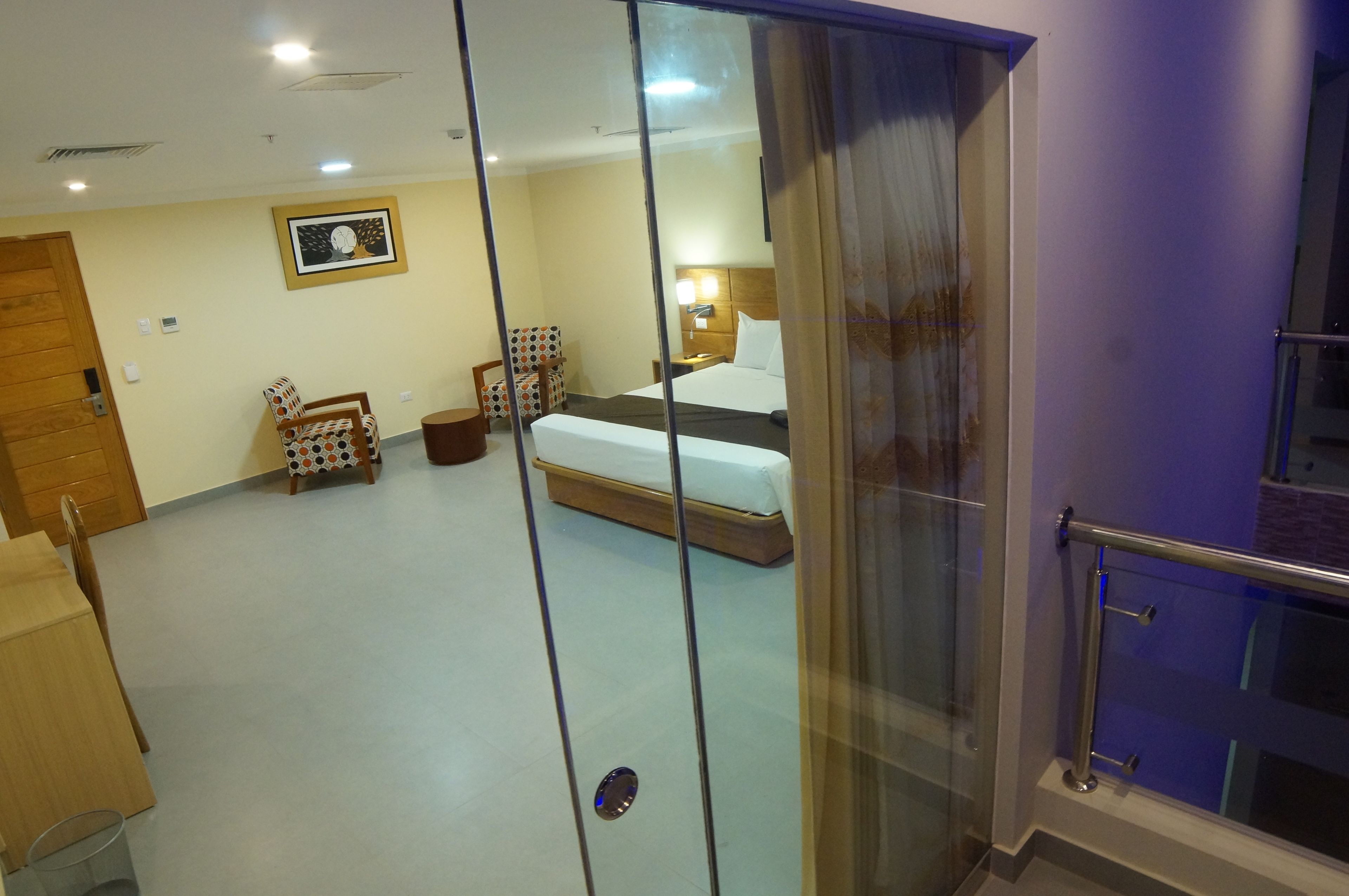 Une chambre d’hôtel avec un lit, une chaise, une petite table et une lampe fixée au mur.