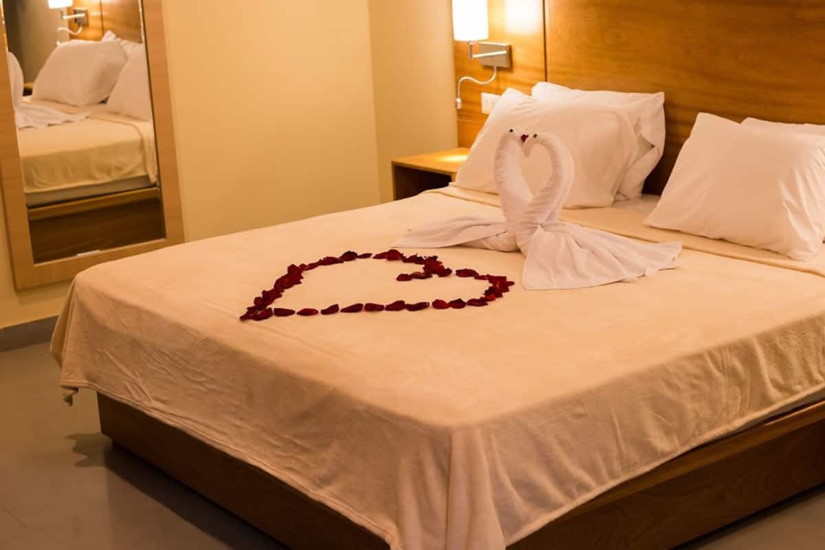 Une chambre d’hôtel avec un lit, une tête de lit en bois, du linge de lit blanc et une décoration en forme de cœur, composée de pétales de roses, sur le lit.