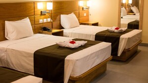 Habitación de hotel con dos camas, cada una con cabecero de madera, ropa blanca y corredor de cama marrón. Hay mesitas de noche con lámparas y un espejo en la pared.