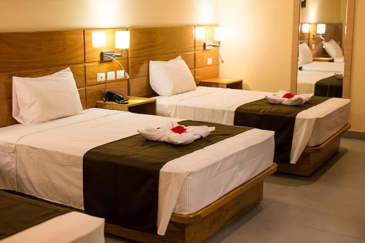 Une chambre d’hôtel avec deux lits, chacun doté d’une tête de lit en bois, de draps blancs et d’un couvre-lit marron. Il y a des tables de chevet avec des lampes et un miroir au mur.