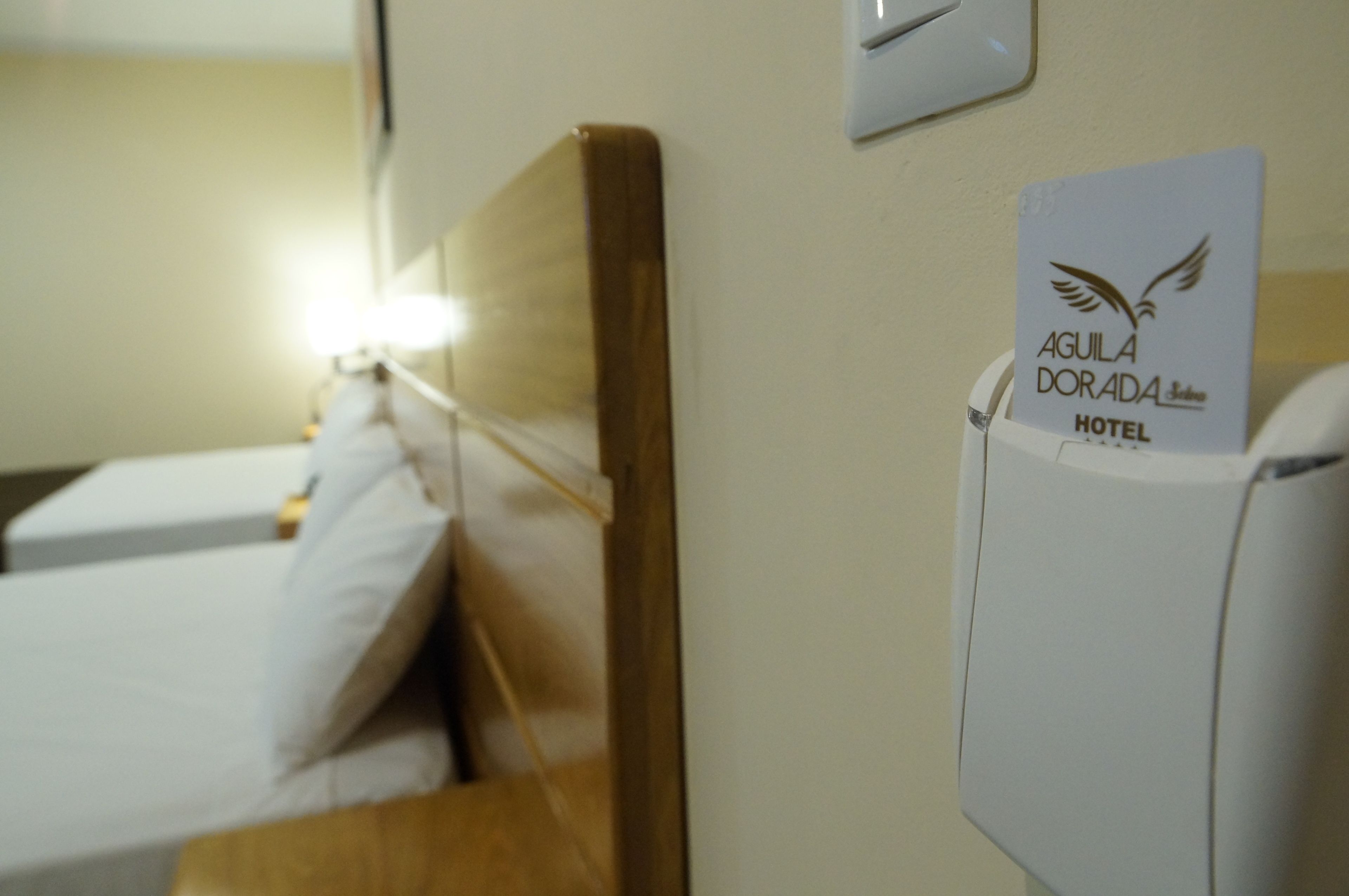 A hotel room with a bed, a wooden headboard, and a sign indicating the hotel name.