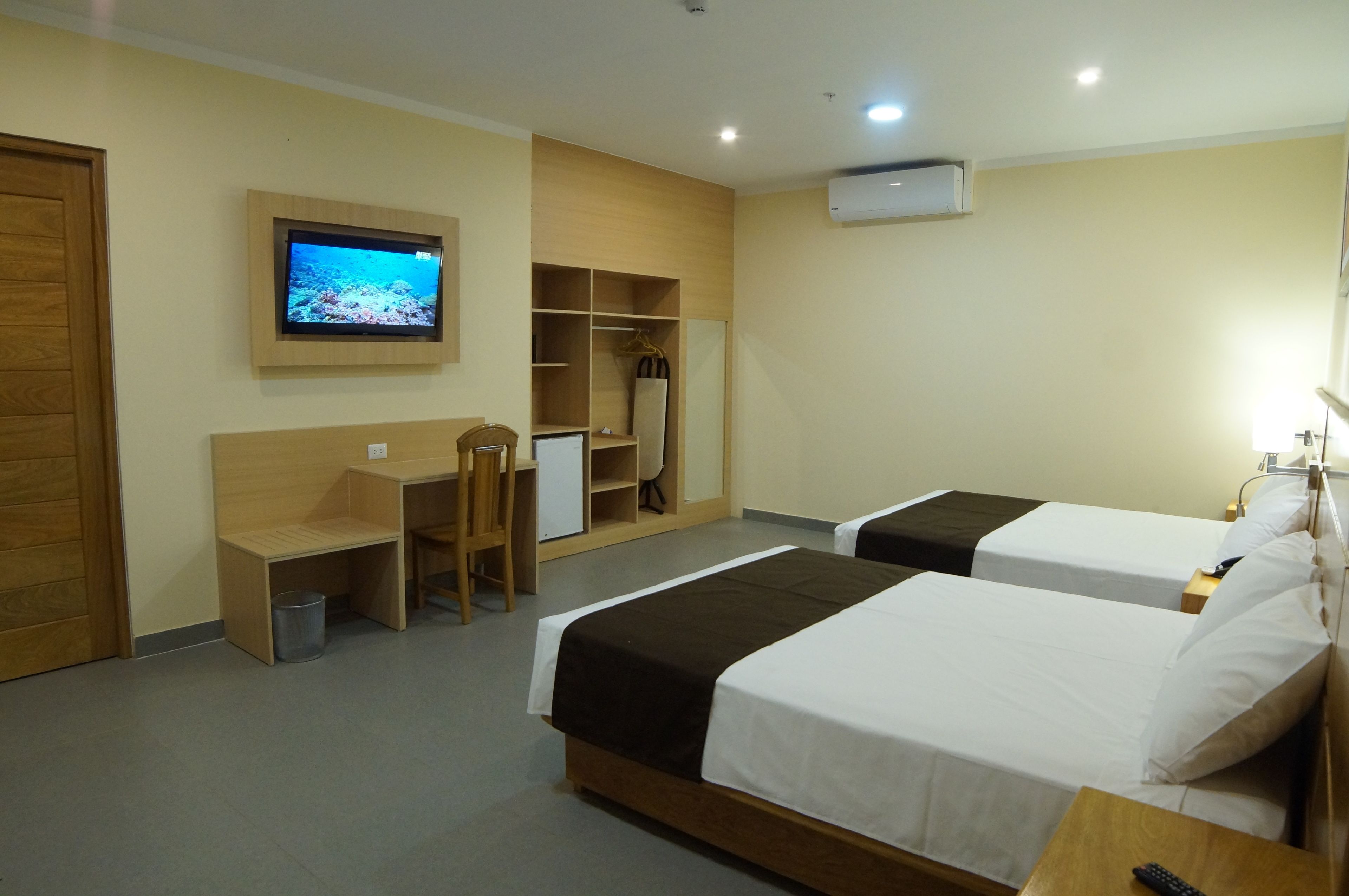 A hotel room with two beds, a desk, a chair, a TV, and a wardrobe.