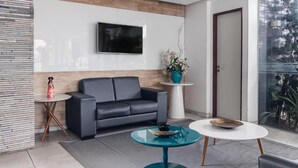 A modern living room with a sofa, a coffee table, and a TV mounted on the wall. - Citi Hotel Express Caruaru (Caruaru)