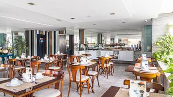 Um restaurante moderno com mesas e cadeiras de madeira, cozinha ao fundo e interior limpo e bem iluminado.